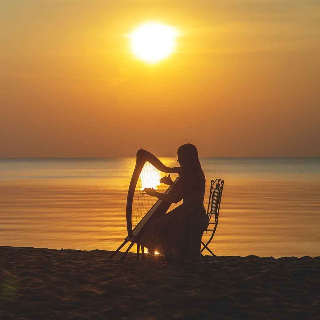 Datos curiosos del arpa, mujer tocando arpa en la playa a contraluz
